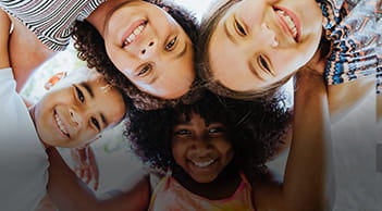 Quatro crianças se abraçam em uma roda e sorriem.