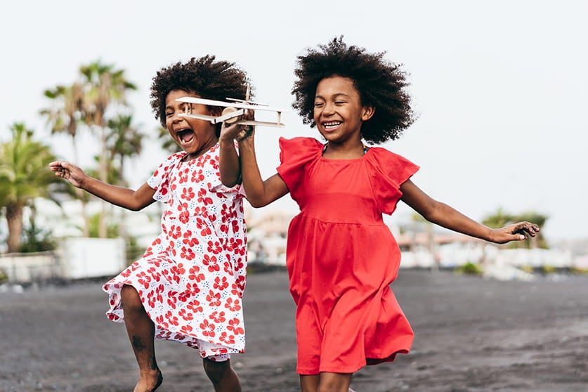 Foto de duas crianças correndo e brincando ao ar livre. Juntas, elas seguram um avião de brinquedo.